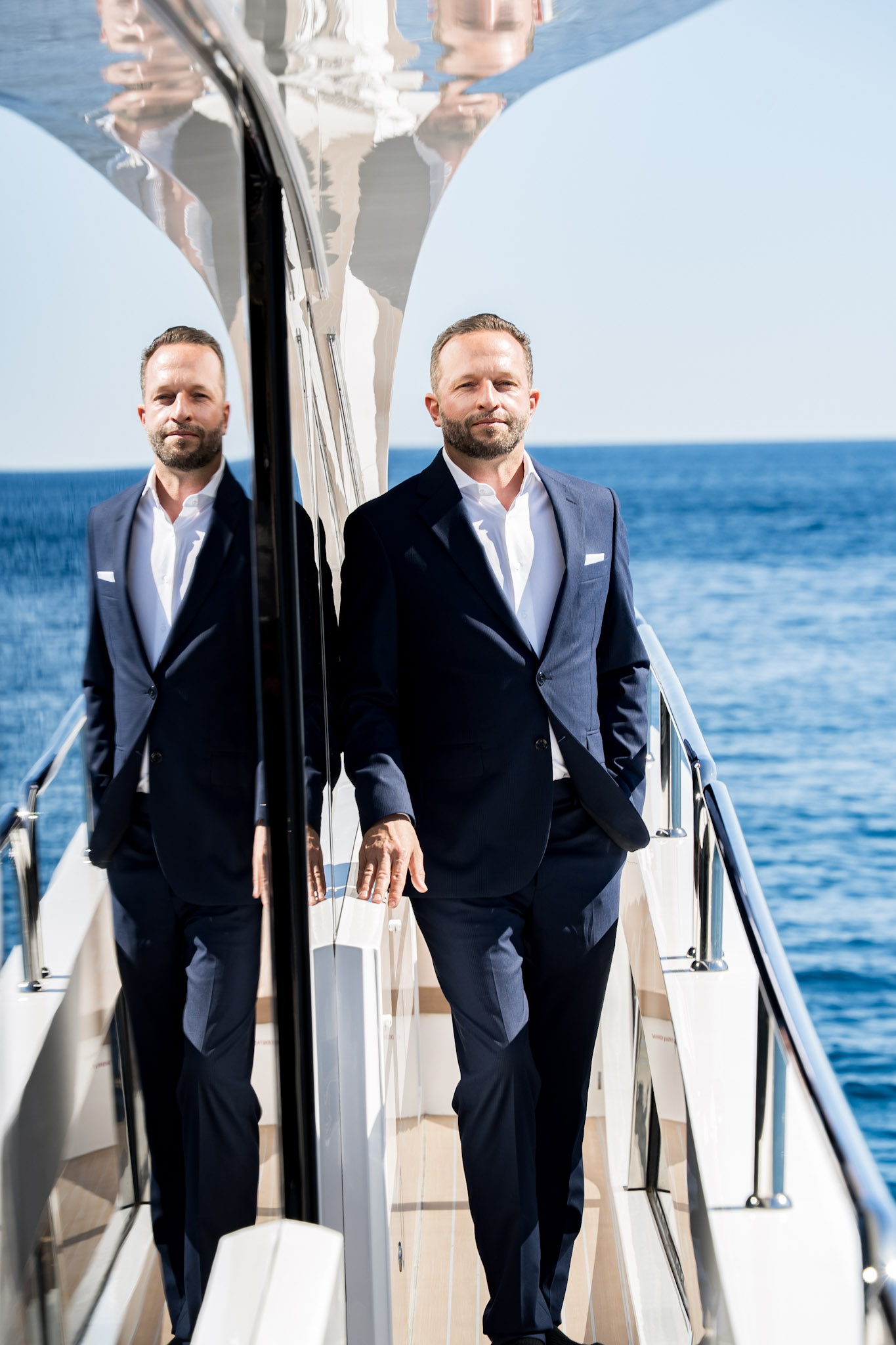 Daniel Rudolf — Butler, Autor und Gründer von Xclusive. Portrait im dunkelblauen Anzug an Deck einer Motoryacht vor dem Mittelmeer.